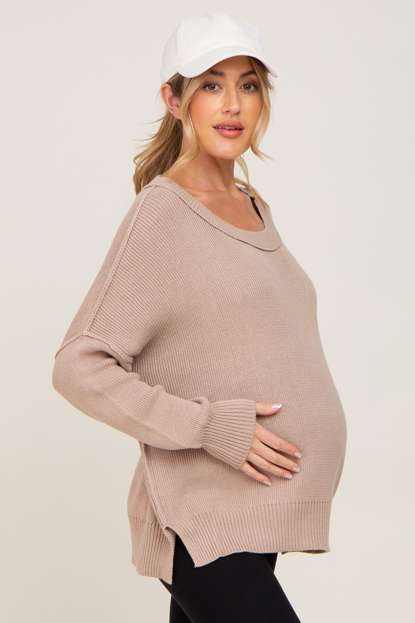 woman wearing a beige maternity sweater with a relaxed fit and side slits, highlighting her baby bump