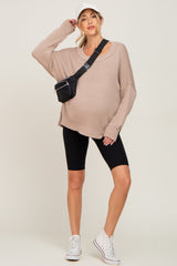 woman wearing a beige oversized maternity sweater, black biker shorts, and white sneakers, with a black fanny pack and cap