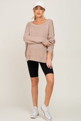 woman wearing a beige oversized maternity sweater and black bike shorts, styled with a white cap and sneakers