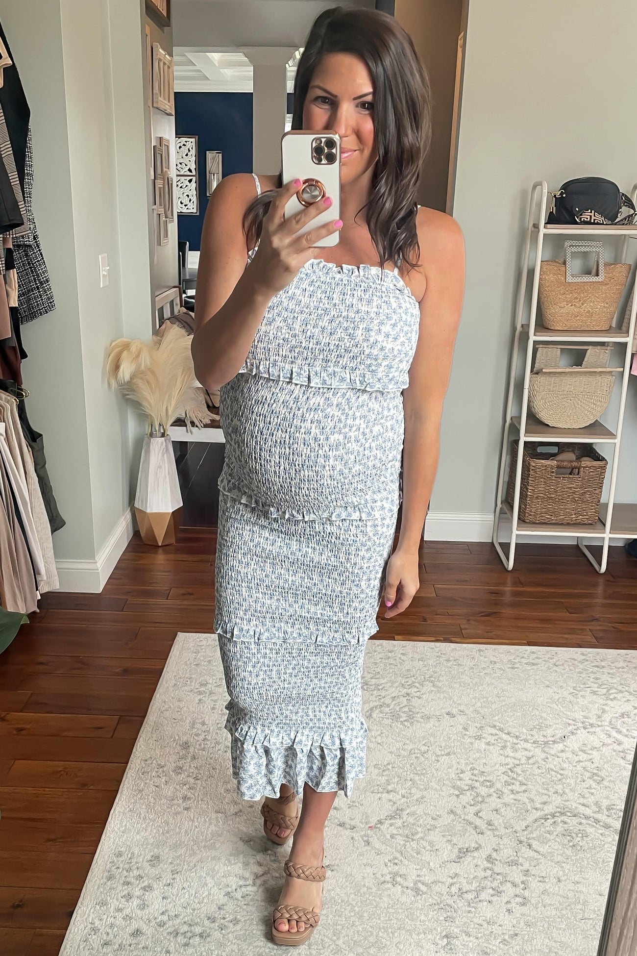 woman wearing a light blue floral strapless maternity dress, showing her baby bump, standing in a stylish room
