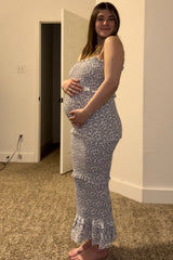woman wearing a light blue floral maternity dress, showcasing her baby bump while standing in a cozy indoor setting