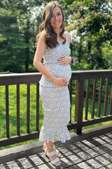 woman wearing a floral maternity dress with ruffles and a baby bump, standing on a deck in natural light
