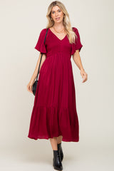 woman wearing a burgundy v-neck midi dress with flutter sleeves and black ankle boots