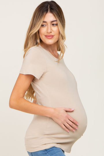 woman wearing a beige short sleeve maternity top and holding her baby bump