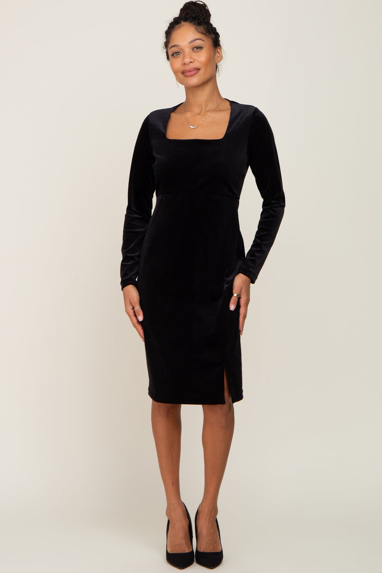 woman wearing a black long sleeve velvet dress with a square neckline and side slit, styled with black high heels