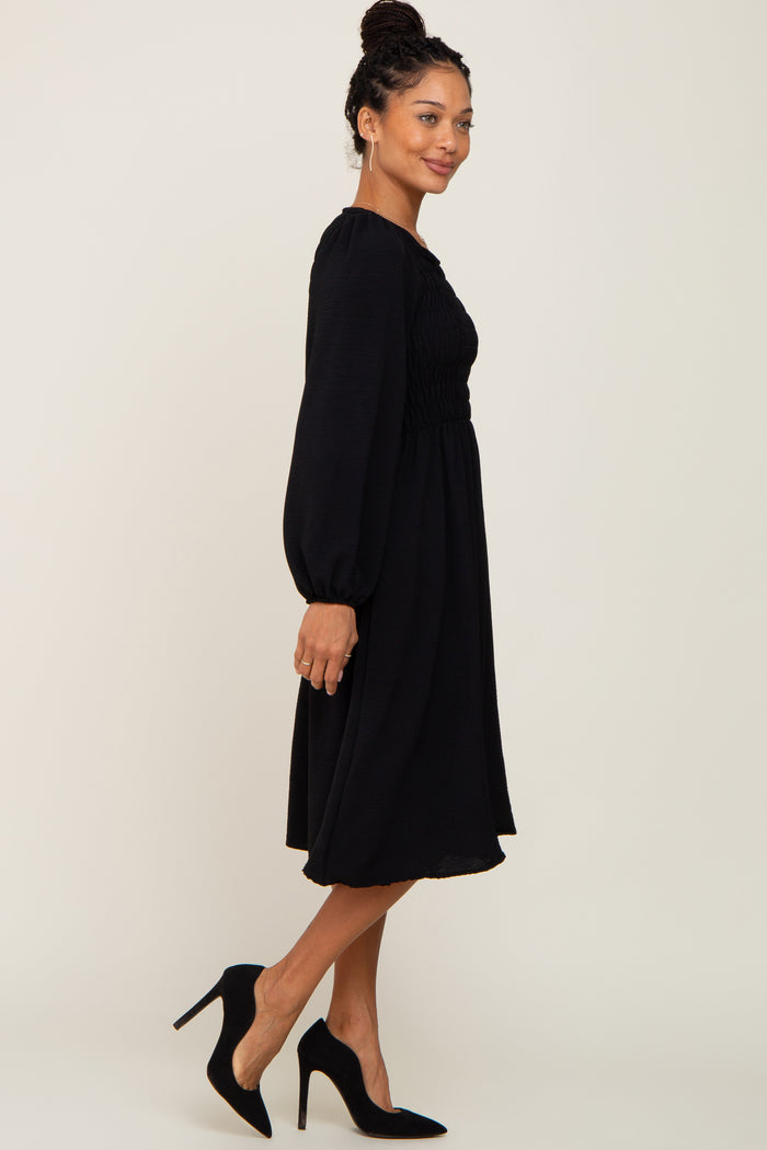 woman wearing a long sleeve black smocked midi dress and black high heel pumps