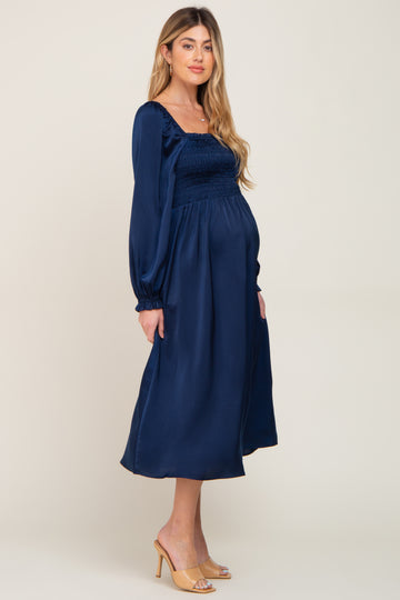 pregnant woman wearing a navy blue long sleeve smocked maternity midi dress and tan heels