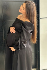 woman wearing a black off-shoulder maternity dress, showing her baby bump while posing outdoors