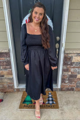 woman wearing a black maternity dress with puff sleeves and a smocked bodice, standing on a welcome mat