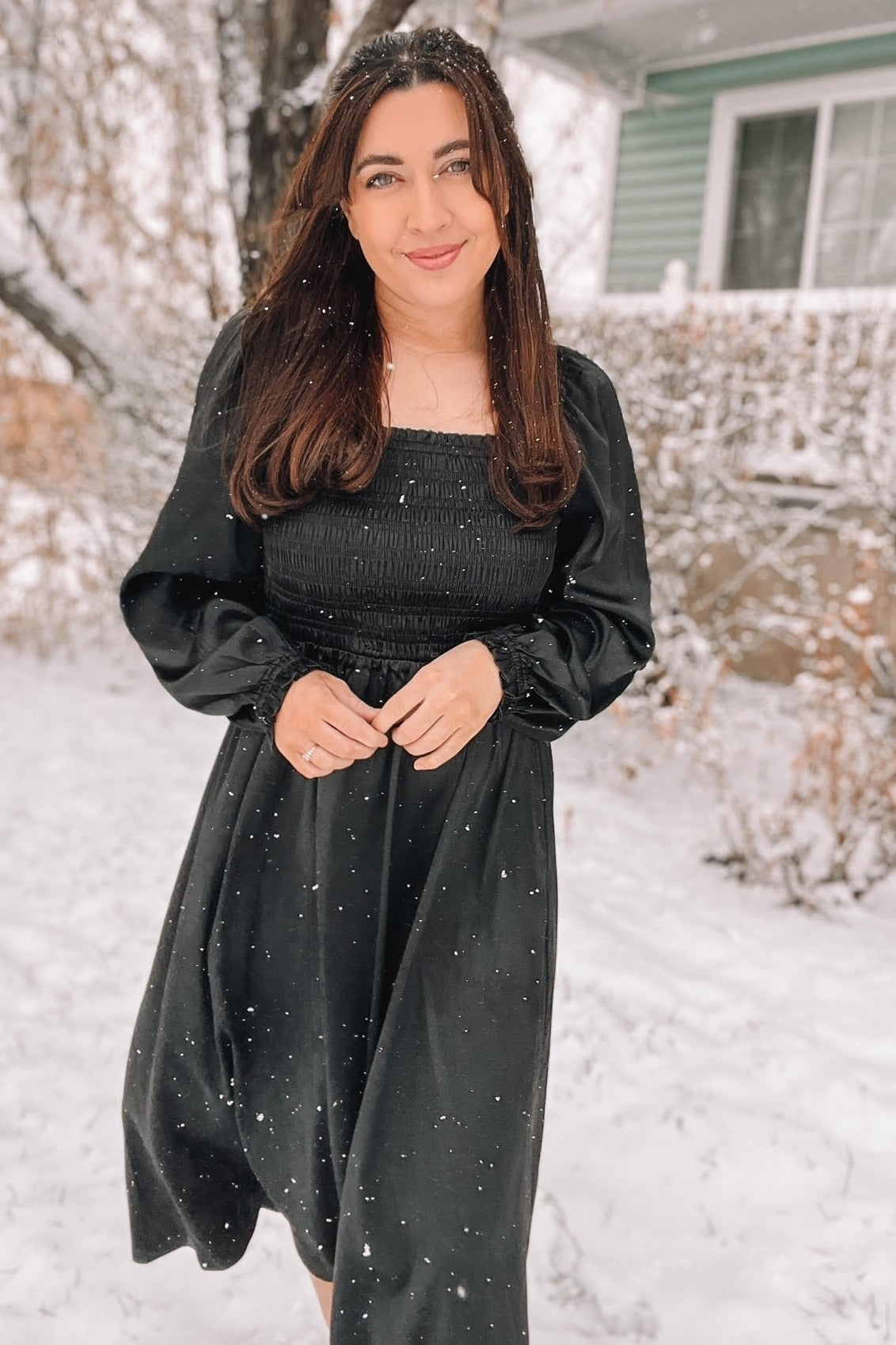 woman wearing a black long sleeve smocked dress standing in the snow with a snowy background