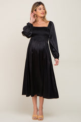 woman wearing a black maternity dress with a smocked bodice and long puff sleeves, showcasing her baby bump