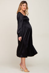 woman wearing a black satin maternity dress with smocked bodice and long sleeves, showcasing her baby bump