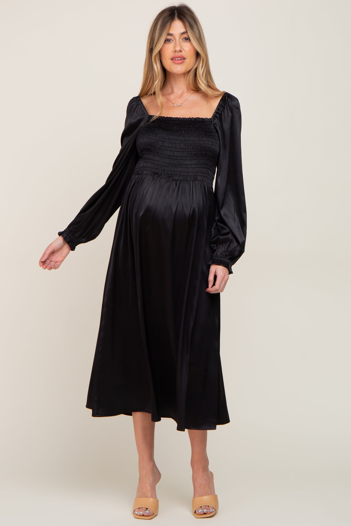 woman wearing a black maternity dress with a smocked bodice and puff sleeves, showing her baby bump
