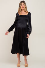 woman wearing a black maternity dress with a smocked bodice and puff sleeves, showing her baby bump