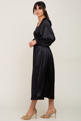 woman wearing a black satin long sleeve midi dress with a smocked bodice and flowing skirt, paired with nude heels