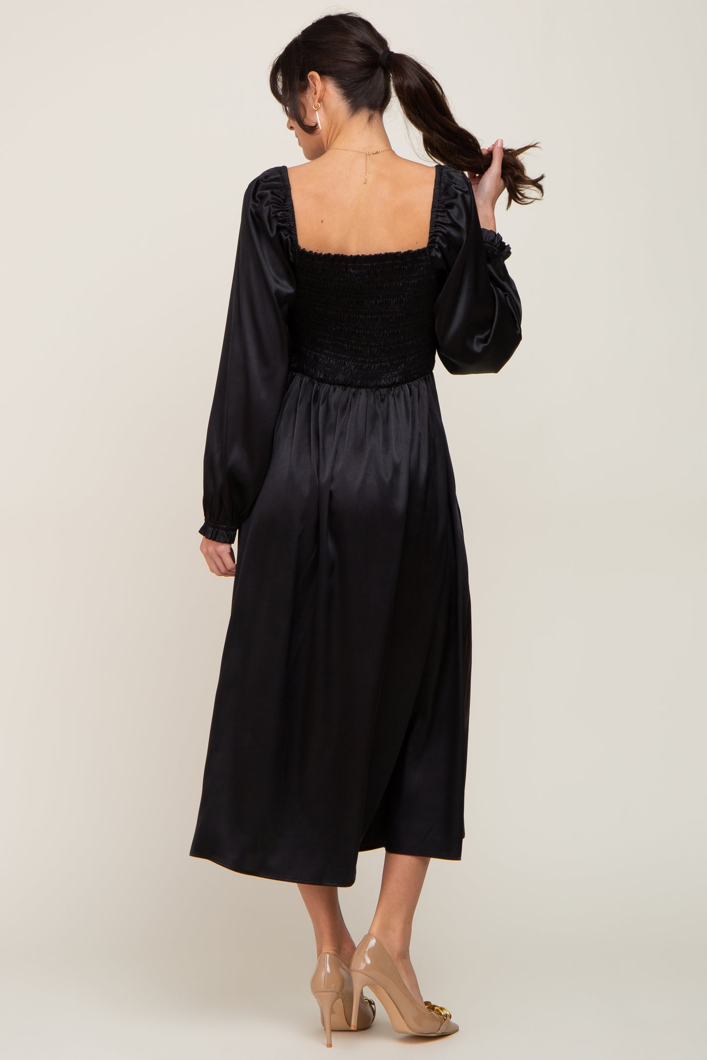 woman wearing a black long sleeve dress with a smocked bodice and a flowy skirt, viewed from the back