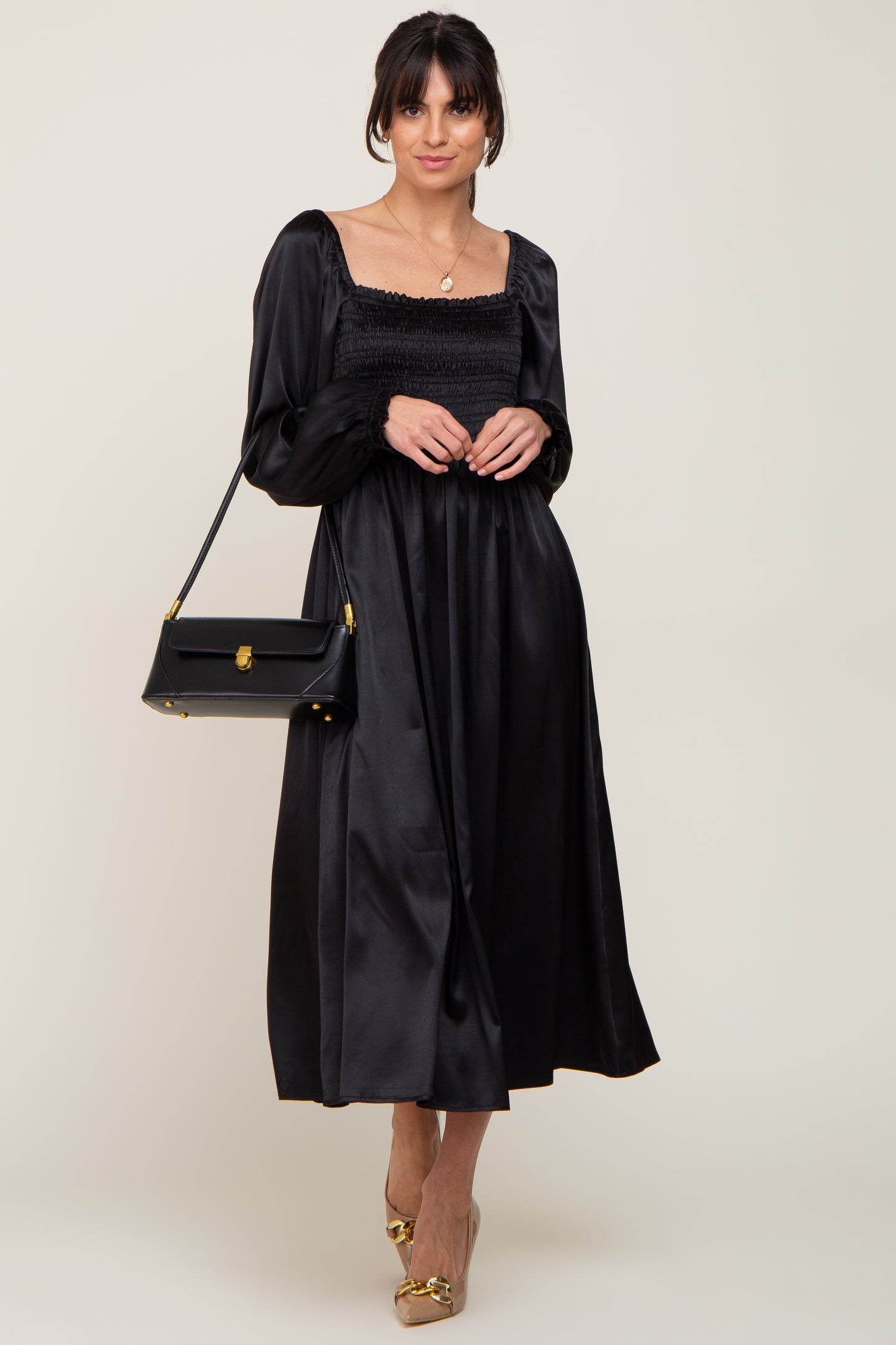 woman wearing a black satin long sleeve dress with a smocked bodice and carrying a black handbag
