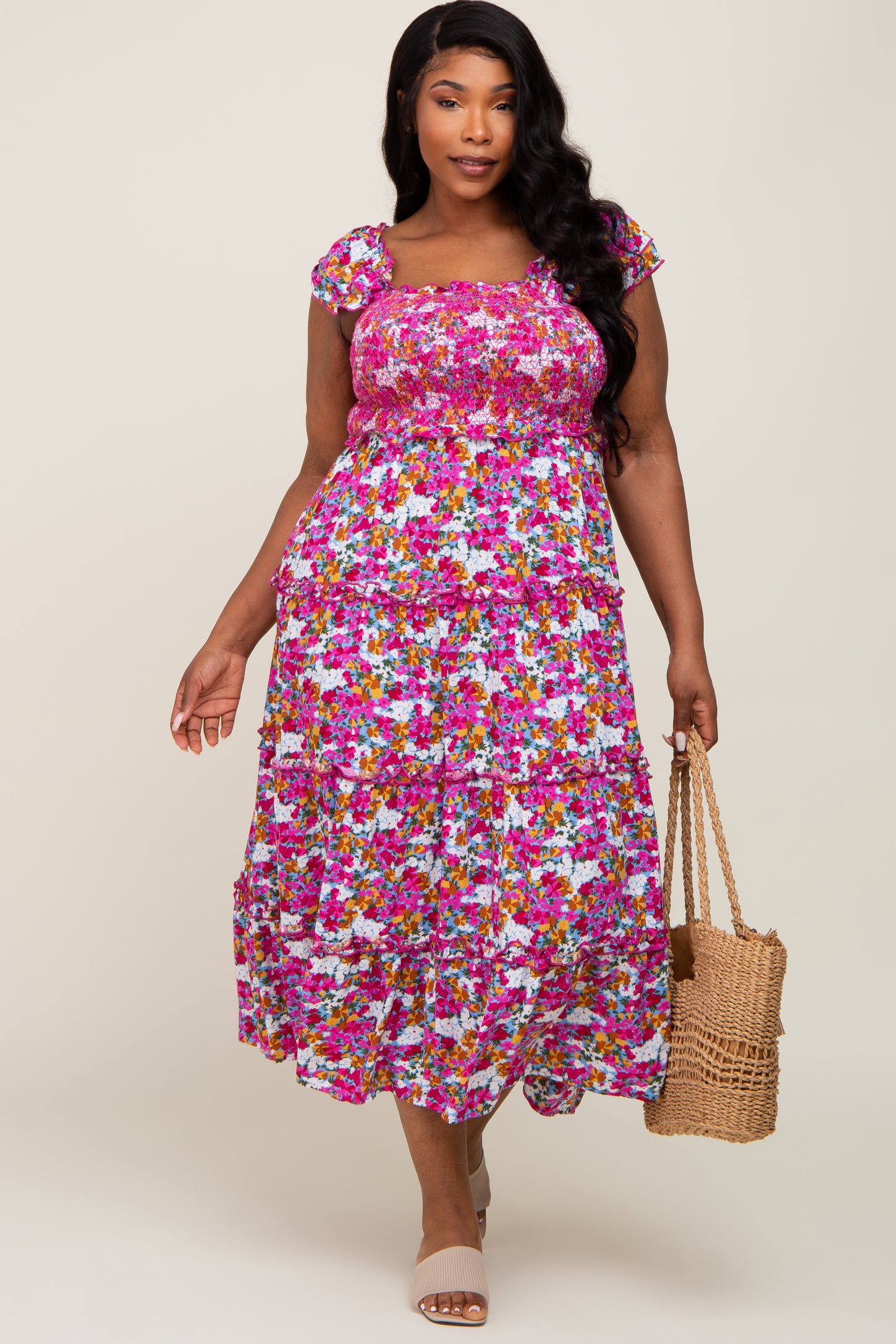 woman wearing a pink floral smocked tiered midi dress and holding a straw tote bag
