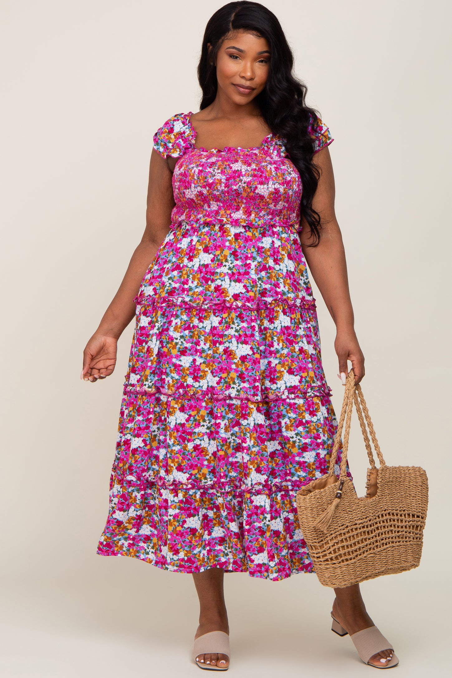woman wearing a floral plus size tiered maxi dress in pink and purple, holding a woven bag