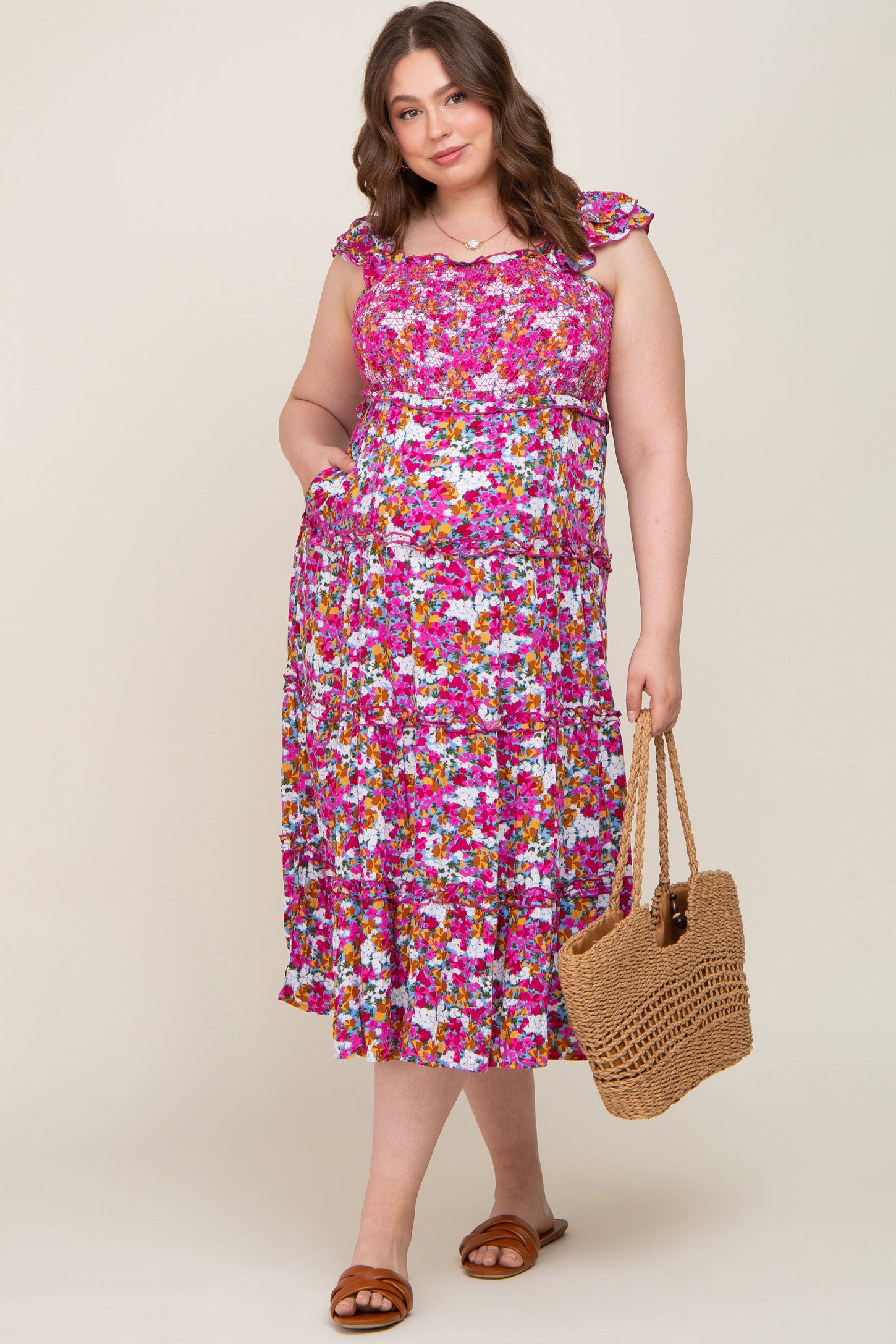 woman wearing a floral maternity plus dress with ruffled sleeves and holding a straw bag, baby bump visible
