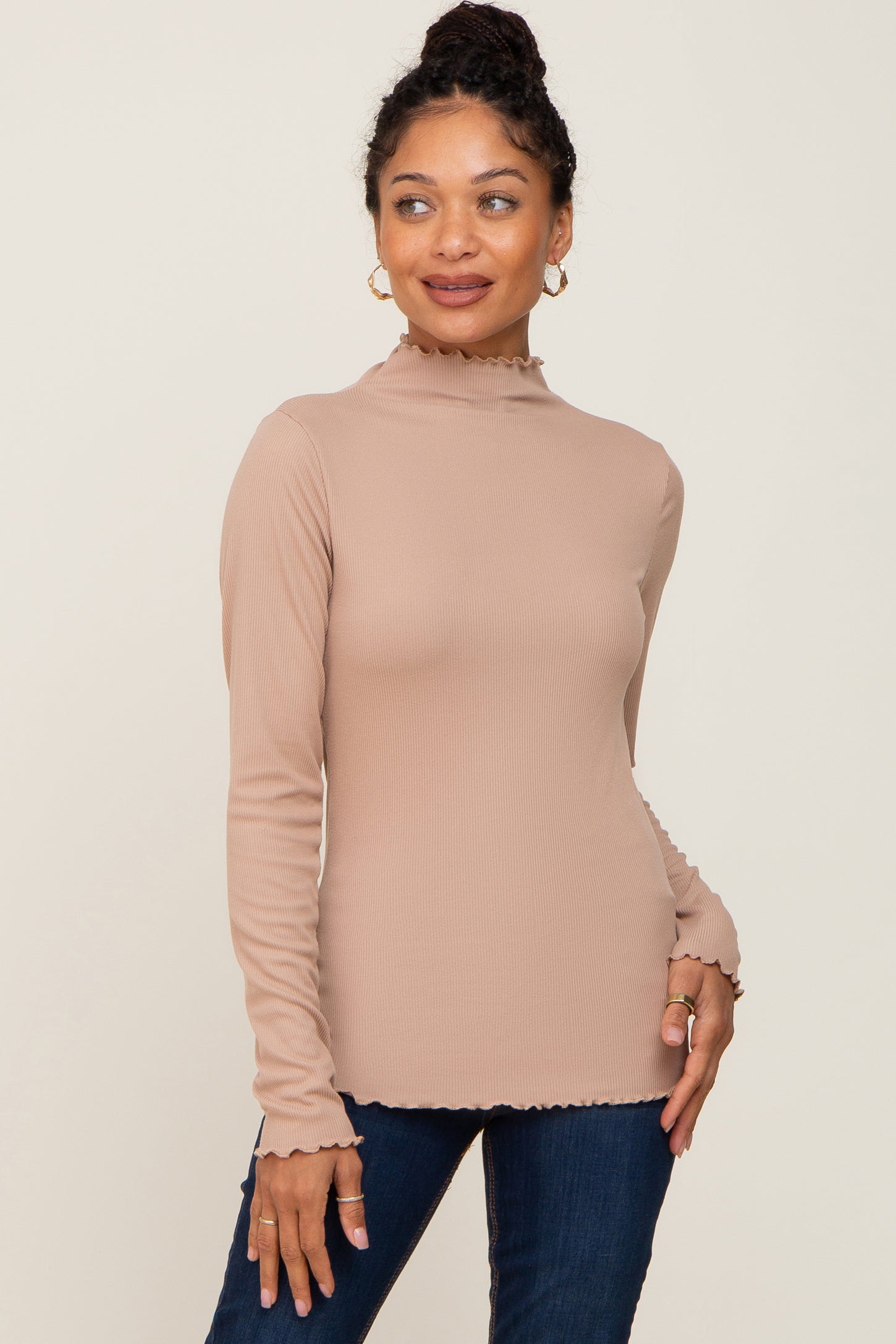 woman wearing a beige long sleeve ribbed top with a mock neck and frill hem details paired with dark jeans