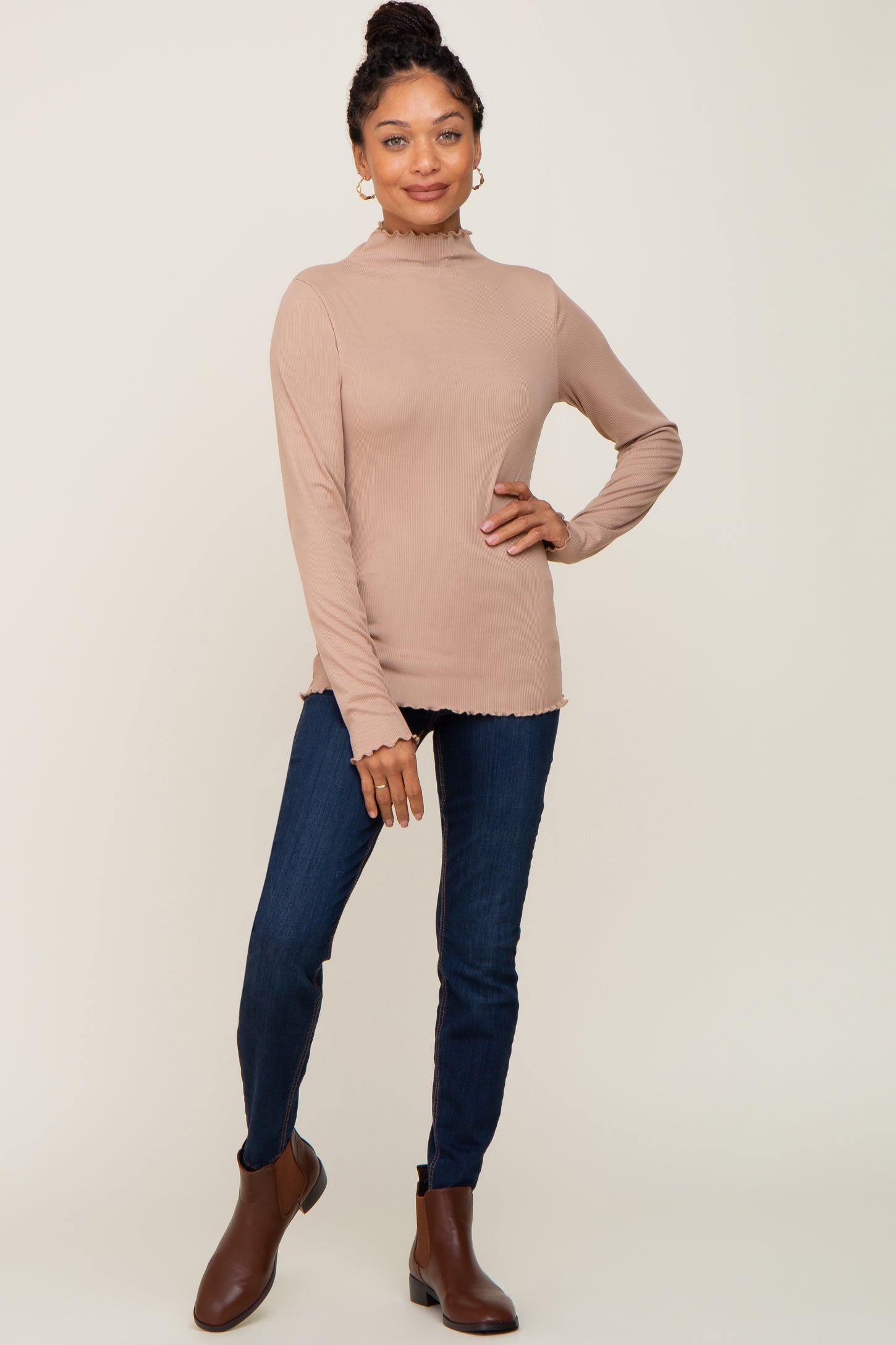 woman wearing a beige ribbed long sleeve top with a mock neck and frayed hem, paired with dark blue jeans and ankle boots