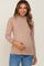 woman wearing a tan long sleeve maternity top with a ruffled neckline and holding her baby bump