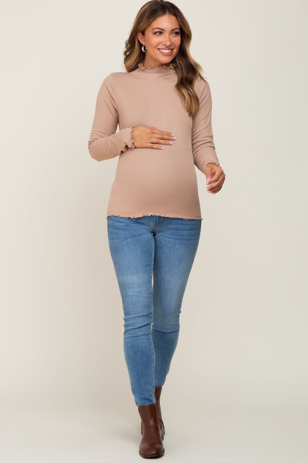 woman wearing a light brown long sleeve maternity top with ruffle details and a baby bump, paired with blue skinny jeans