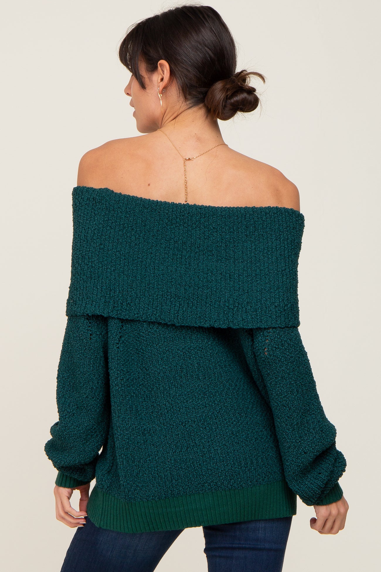 Woman wearing a dark green off-the-shoulder knit sweater with a fold-over neckline and long sleeves