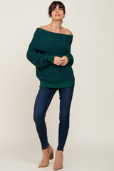 Woman wearing a dark green off-the-shoulder knit sweater, dark blue skinny jeans, and tan suede ankle boots.