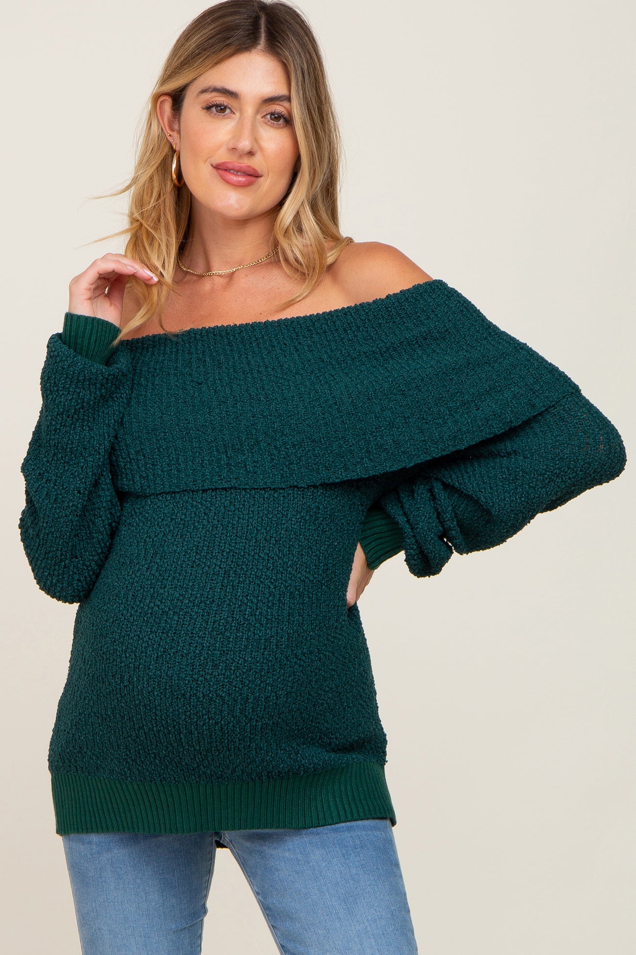 woman wearing a dark green off-the-shoulder maternity sweater and blue jeans