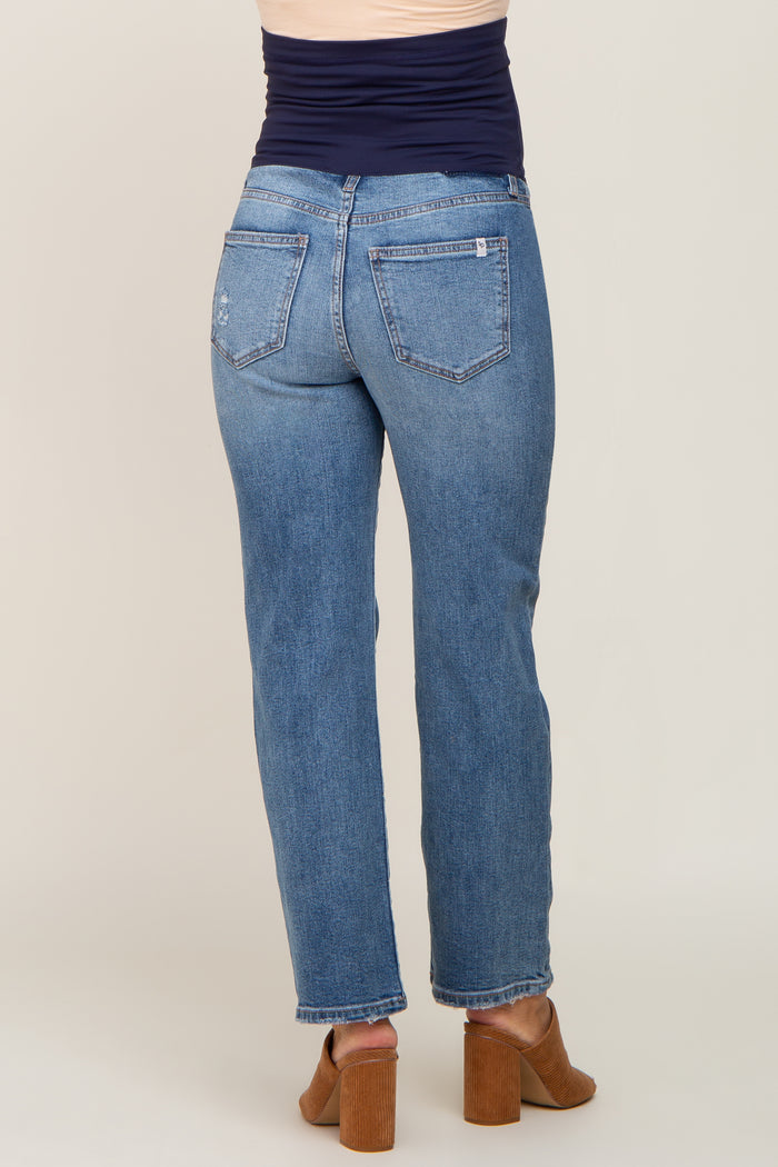 Back view of woman wearing blue straight leg maternity jeans with a navy belly band and brown heeled mules