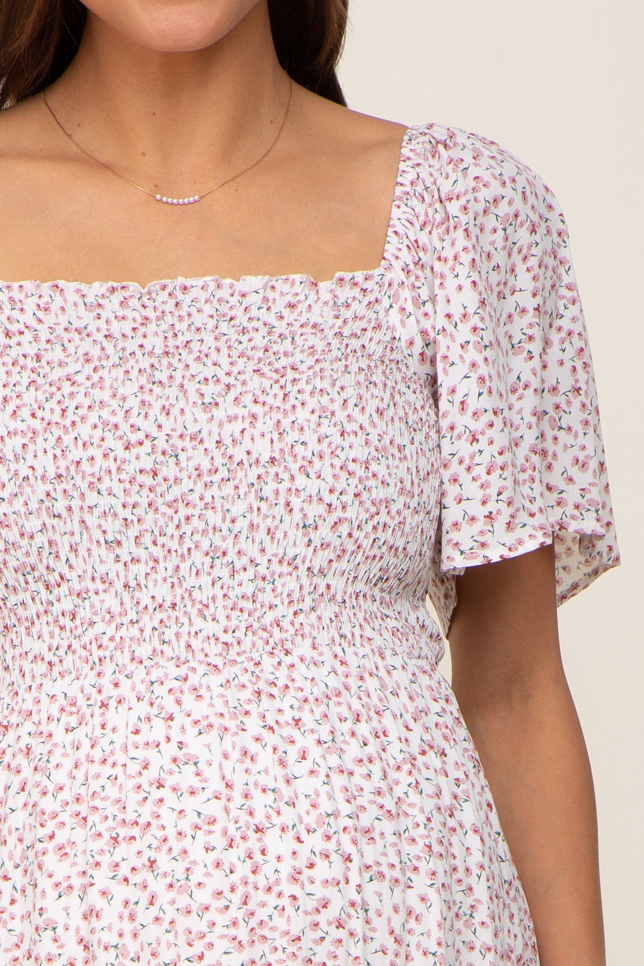 Close up of a woman wearing a white smocked maternity dress with a pink floral print and flutter sleeves