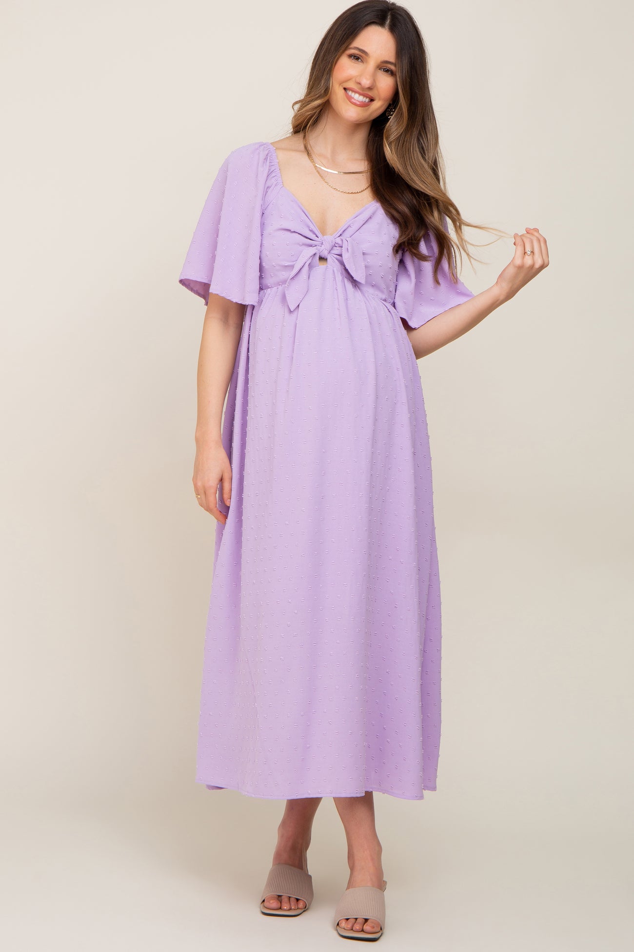 woman wearing a lavender maternity dress with short flutter sleeves and a tie detail, showcasing her baby bump