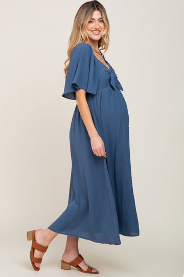 woman wearing a blue maternity dress with flutter sleeves and a bow detail, showing her baby bump