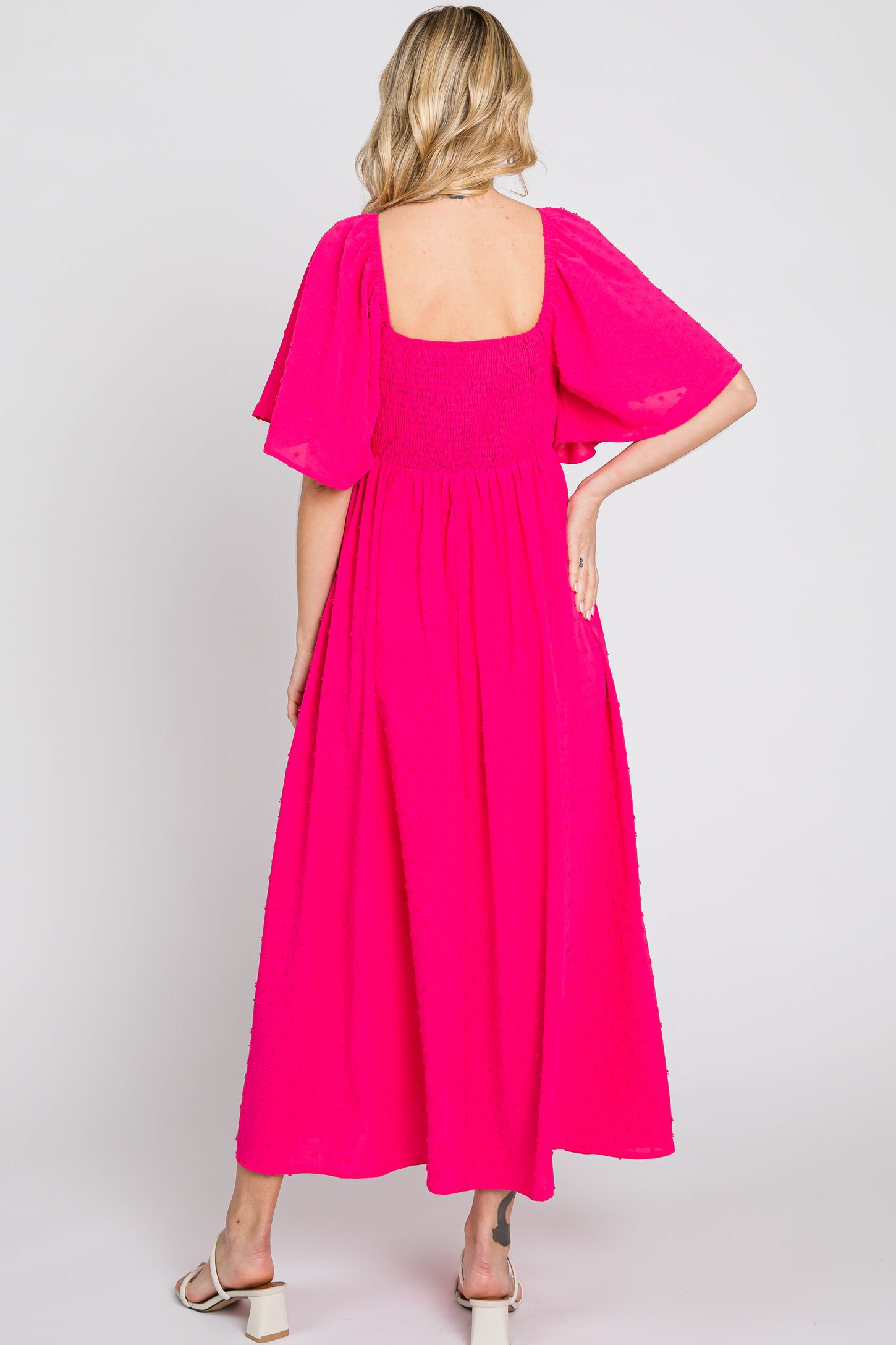 woman wearing a hot pink maxi dress with smocked bodice and flutter sleeves, shown from the back
