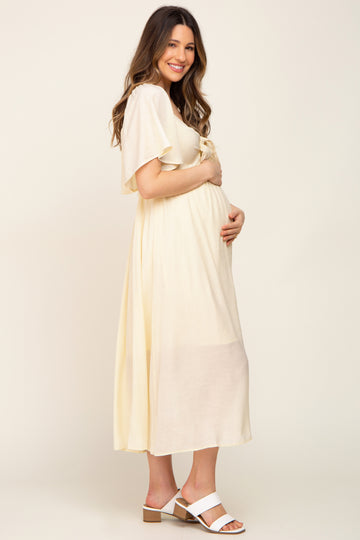woman wearing a light yellow maternity dress with flutter sleeves and holding her baby bump