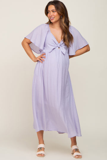 woman wearing a lavender maternity maxi dress with flutter sleeves and a bow detail, showcasing her baby bump
