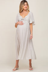 woman wearing a light gray maternity dress with a tied front and flutter sleeves, holding her baby bump