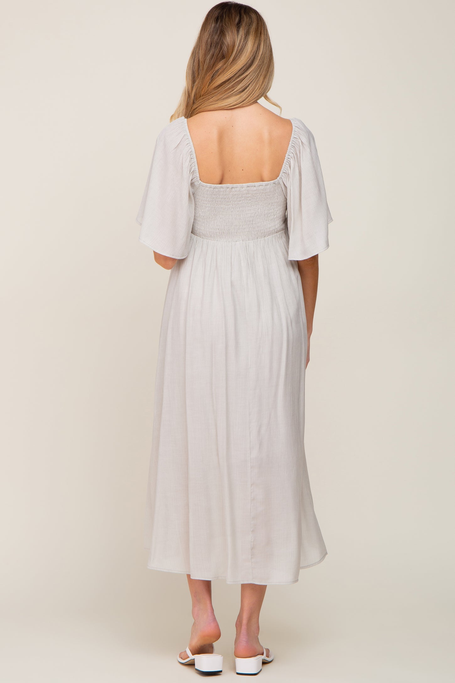 woman wearing a light gray maternity dress with flutter sleeves and a smocked bodice, showing a baby bump from the back