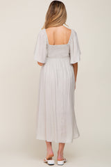 woman wearing a light gray maternity dress with flutter sleeves and a smocked bodice, showing a baby bump from the back