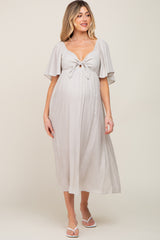 woman wearing a light gray maternity dress with a tie front and flutter sleeves, showcasing her baby bump