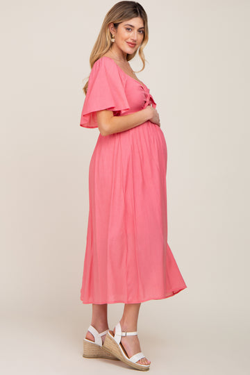 Pregnant woman in a pink flutter sleeve maternity midi dress and white wedge sandals