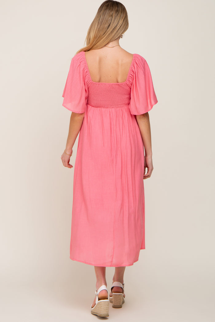 woman wearing a pink maternity dress with short flutter sleeves and a smocked bodice, showing a baby bump