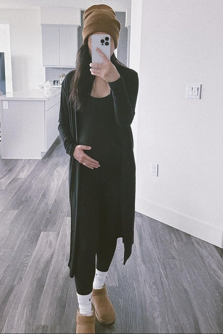 woman wearing a black maternity cardigan and holding her baby bump in a cozy home setting