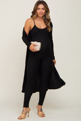 woman wearing a black ribbed maternity jumpsuit with a matching long cardigan and holding a clutch, showing baby bump