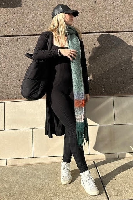 woman wearing a black ribbed maternity outfit with a long cardigan and carrying a black bag, accessorized with a colorful scarf and sneakers
