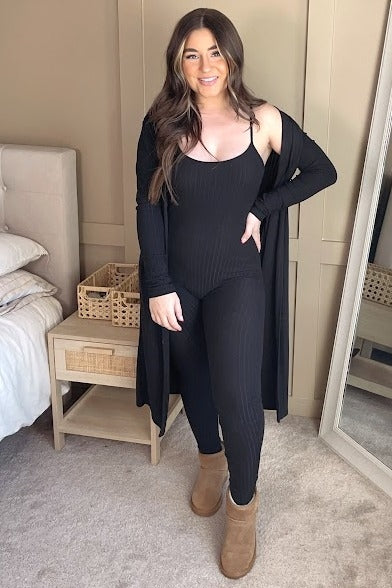 woman wearing a black ribbed maternity jumpsuit with a matching long cardigan and brown ankle boots, showcasing her baby bump