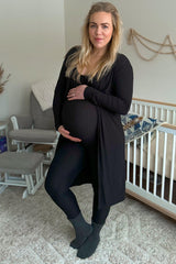 woman wearing a black maternity cardigan and leggings, holding her baby bump while standing in a nursery