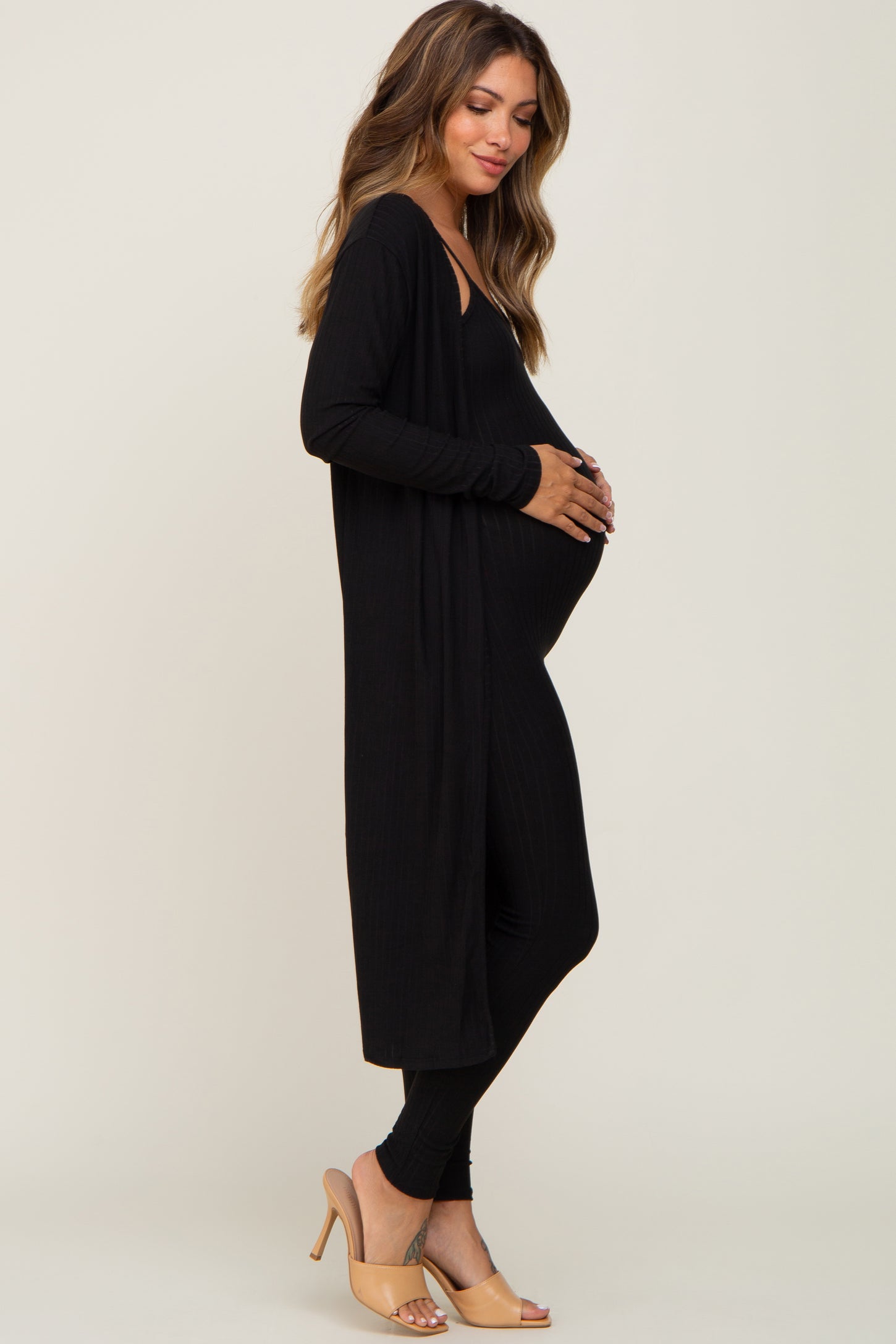 woman wearing a black long sleeve maternity cardigan over a black maternity jumpsuit and holding her baby bump